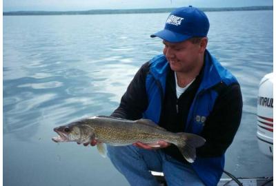 man holding walleye close to boat motor water in background is clear blue