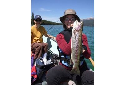 girl sitting in boat holds up a rainbow trout 