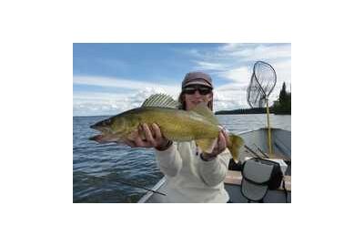 woman sitting in boat holds a walleye close to her face with both hands