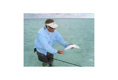 man standing in water wearing shorts and no waders holding a fish and fishing rod