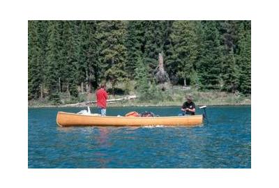 two men on opposite ends of a long boat in lake with coniferous forest in the background