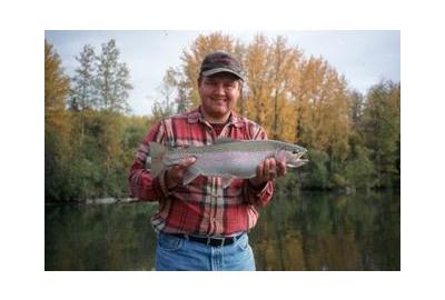 man holding rainbow trout trees and lake in the background