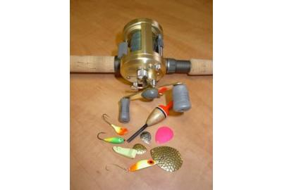 close up of reel on fishing rod and a variety of lures and bait on a wooden surface