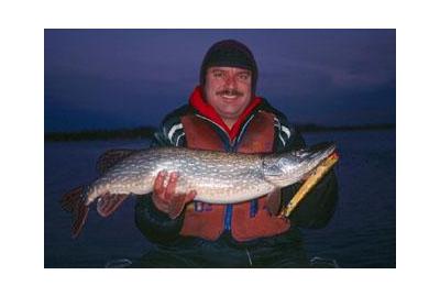 man holding big pike at night