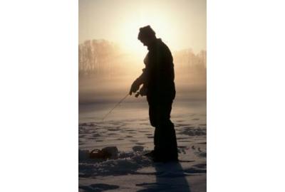 silhouette of man standing up ice fishing with bright warm sunlight behind him