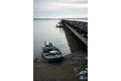 vertical shot of small fishing boat next to a large wooden dock sky is cloudy and nearly sunset