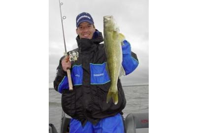 standing man holds a fishing rod in his right hand and a medium size fish with his left