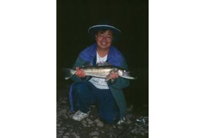 man kneeling down in the dark smiling holding medium to large fish