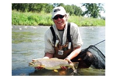 man wearing waders squats in water and holds fish next to a net