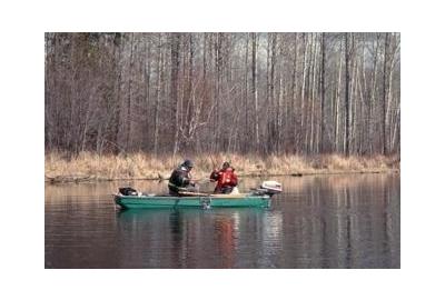 two men sitting in green boat during early spring catching fish with net