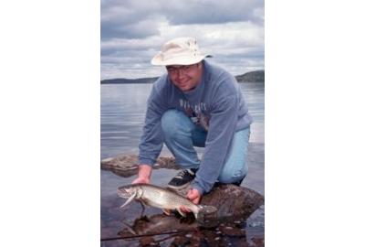 kneeling man holding fish on rocky shore