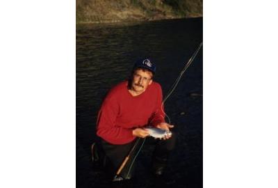 guy kneeling on one knee holding small fish in palm on hand and fishing pole leaning on his left arm