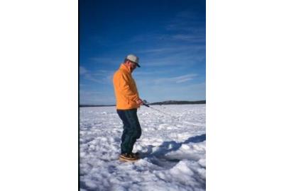 man wearing yellow jacket and jeans ice fishing in the snow