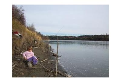 young girl sitting on ground by river stream playing with wooden stick