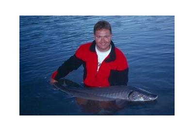 man holding large sturgeon standing in lake