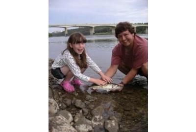 young girl and man squatting by near river stream holding small fish