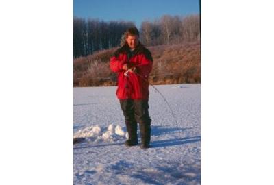 man standing in snowy field holding fishing rod downwards