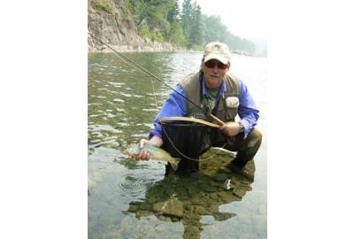 man squatting in shallow water holding fish in right hand and fishing rod in left