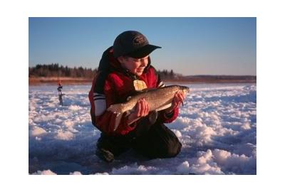 young boy sitting on snow holding fish during sunset