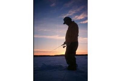 man standing on ice during sunset holding fishing rod