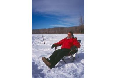 man sitting on camping chair on the snow covered ice 