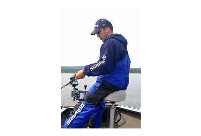 man sits on cushioned boat stool gripping onto fishing rod with left hand