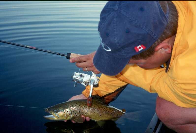 man kneeling and holding caught pike by water