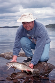 kneeling man holding fish on rocky shore