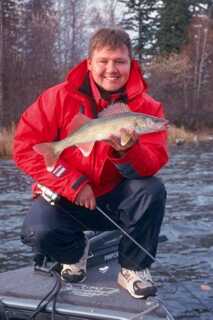 kneeling man in red jacket holding walleye with one hand and fishing rod in the other