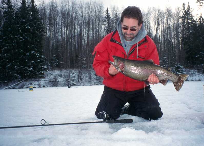 man holding fish and kneeling on snow behind fishing rod