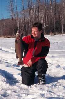 man kneeling on one knee on snow holding fish vertically 