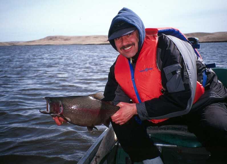 man with a life vest squatting on edge of boat holding medium size fish