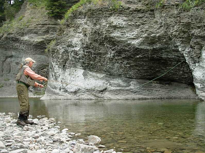 man standing on rocky shore casts line by large stone caverns