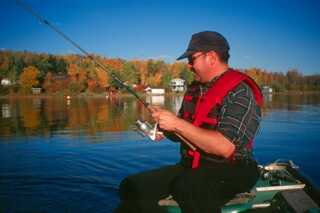 man sitting in boat wearing sunglasses and red life vest fishing with rod in hand