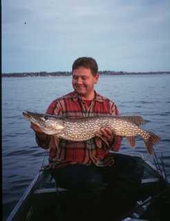 man wearing flannel shirt holds large fish with both hands sitting in boat