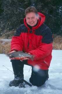 man holding brook trout on ice outdoors red jacket winter 