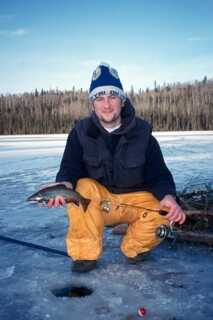 man crouching down on ice holding fishing rod and fish 