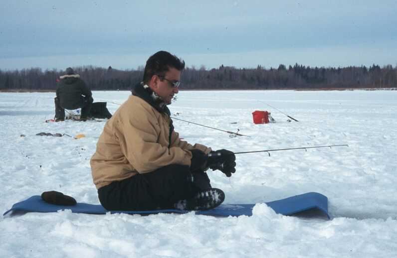 man ice fishing sitting on mat or sled 