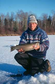 man in toque and sweater kneeling holding fish with both hands