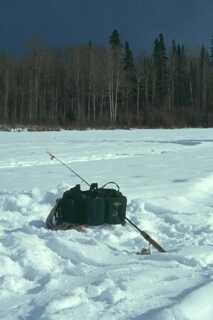 fishing gear bag on set on snowy ground with fishing rod leaning against it