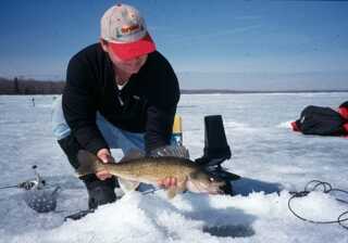 man squatting by ice fishing hole surrounded by gear holding fish