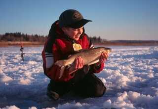 young boy sitting on snow holding fish during sunset