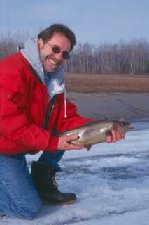 man hearing sunglasses and red jacket on one knee holding rainbow trout with bare hands