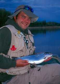 man wearing fishing vest and hat sitting in boat holding fish