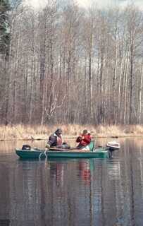 two people sitting in a small green boat on a lake in early spring