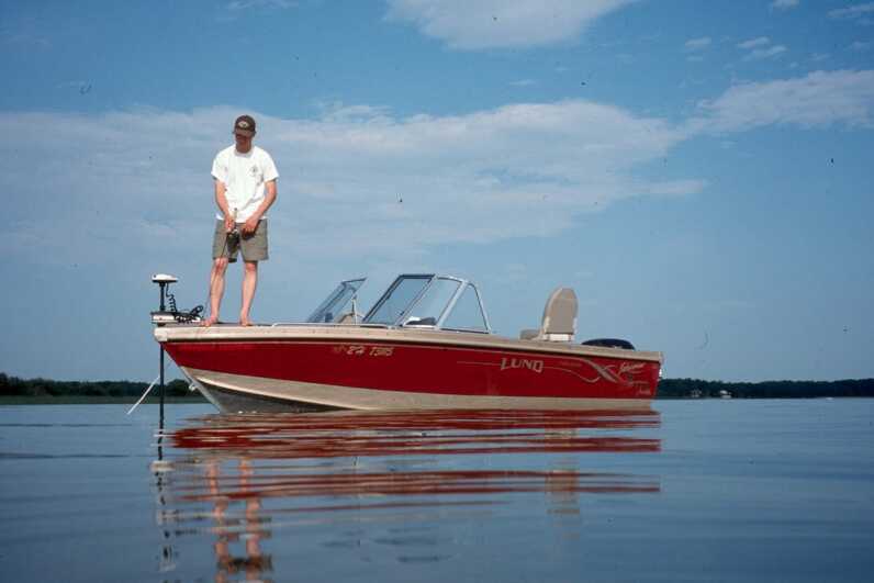 man standing at the front tip of red boat in middle of water 