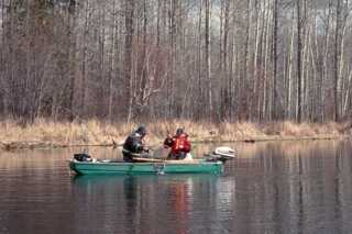 two men sitting in green boat during early spring catching fish with net