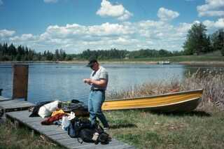 man standing between dock and yellow boat next to pile of bags and supplies