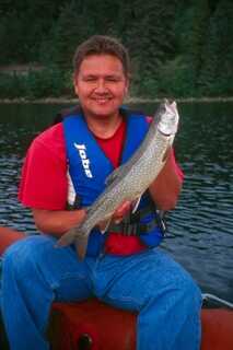 Man wearing blue life vest holding medium size fish sitting on edge of boat 