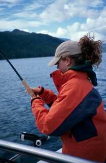 woman looking to the right towards water holding up fishing rod